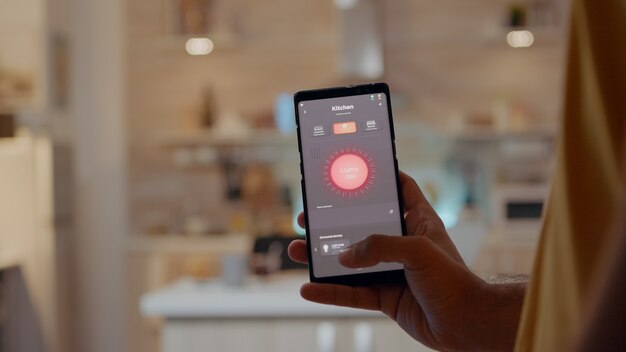 Young man using smart home application software touching screen to turn on the light by mobile phone