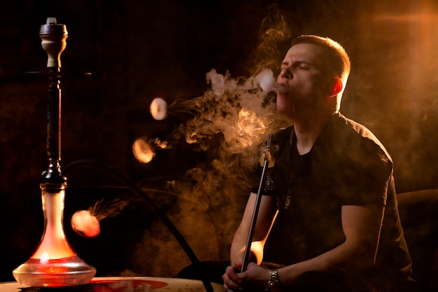 Young man vaping from a hookah in a bar