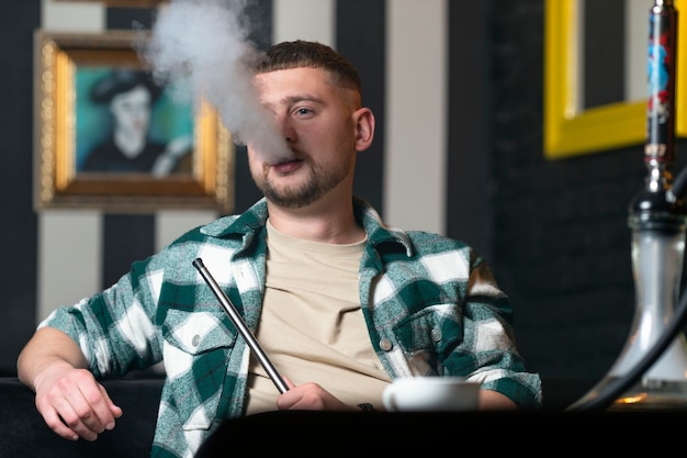 Free photo young man vaping from a hookah in a bar