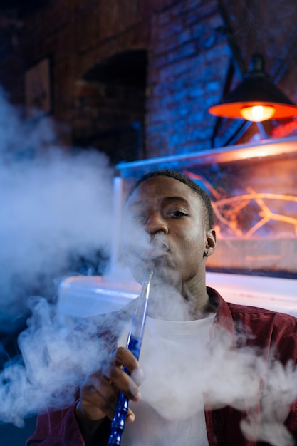 Young man vaping from a hookah in a bar