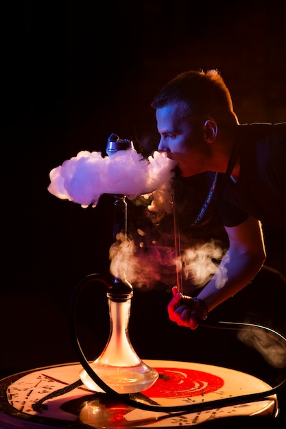 Young man vaping from a hookah in a bar