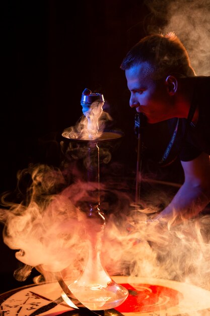 Young man vaping from a hookah in a bar