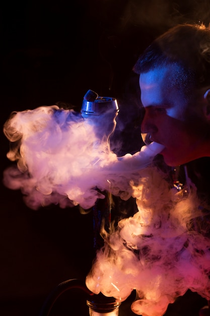 Young man vaping from a hookah in a bar