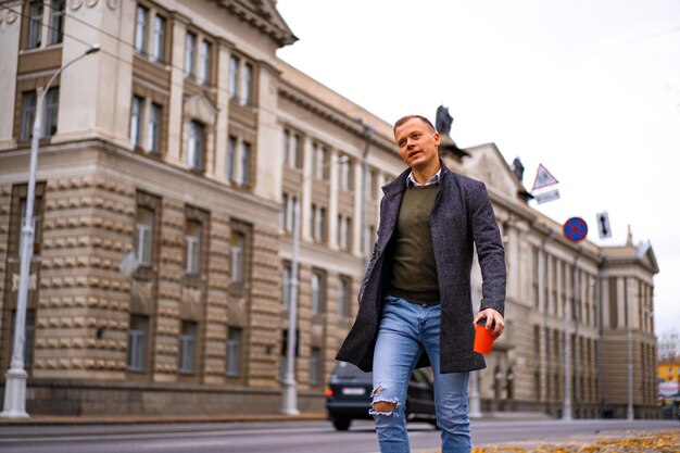 Young man walking in the autumn city with a glass of coffee