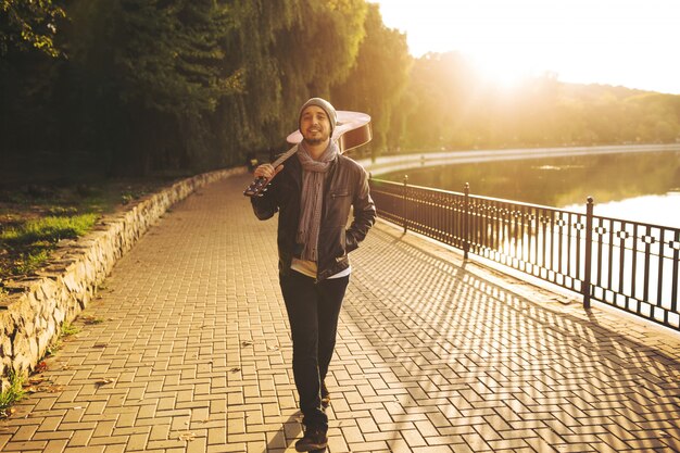 Young man walks by the lake and holding guitar