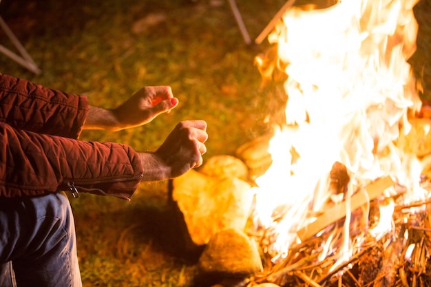 Free photo young man warming up his hands above the bonfire. campsite in the mountains.