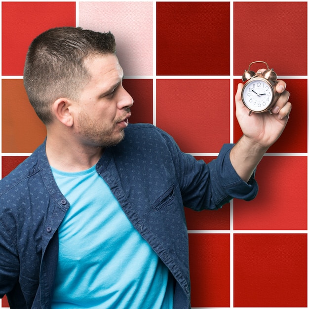 Young man wearing a blue outfit. Holding a clock. Looking to it.