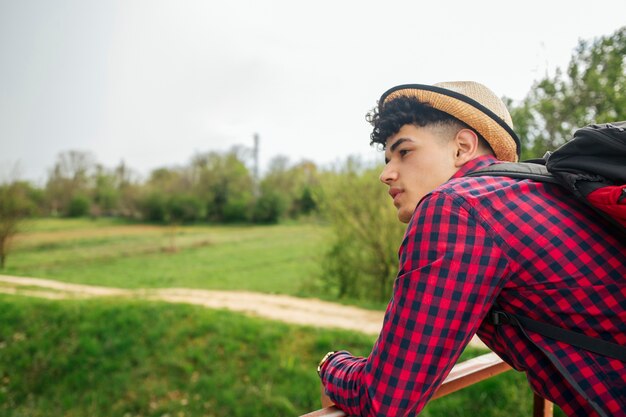 Young man wearing hat carrying backpack looking away