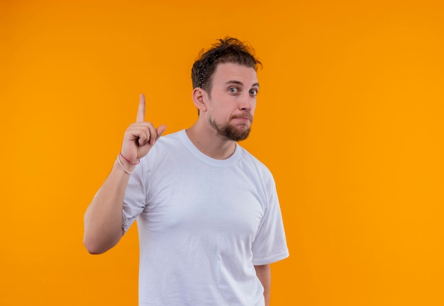  young man wearing white t-shirt points to up on isolated orange wall