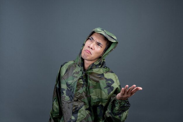 The young man wears a camouflage raincoat and shows different gestures. 