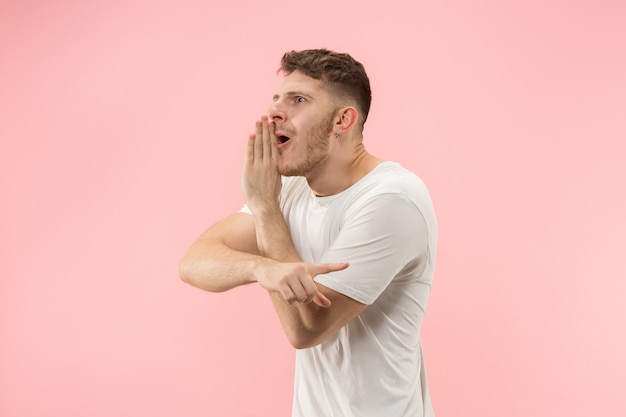 The young man whispering a secret behind her hand over pink background