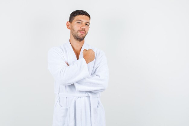 Young man in white bathrobe keeping fist clenched and looking confident , front view.