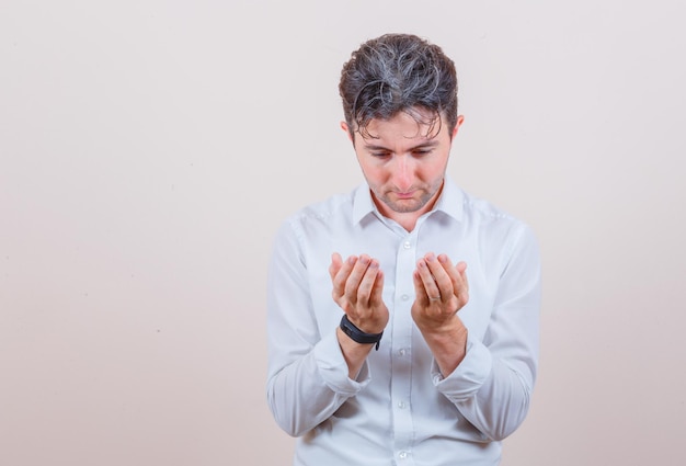 Young man in white shirt holding hands in praying gesture and looking hopeful