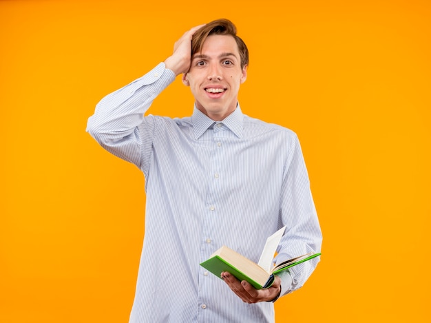 Free photo young man in white shirt holding open book looking  smiling cheerfully being surprised standing over orange wall