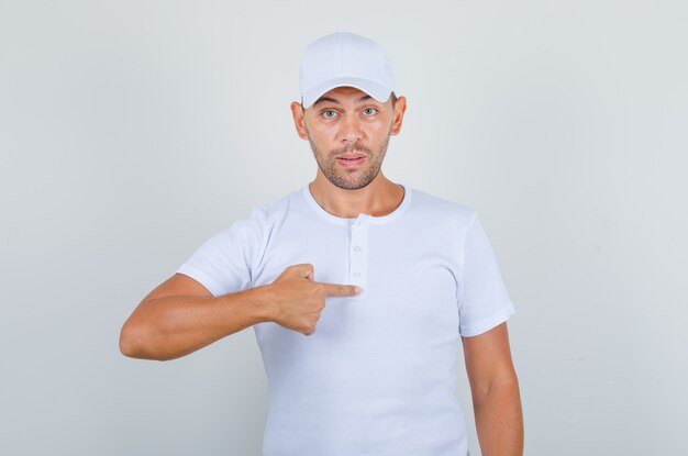 young man in white t-shirt, cap showing finger like asking Me and looking surprised,front view.