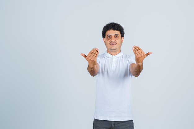 Young man in white t-shirt, pants inviting to come and looking confident , front view.