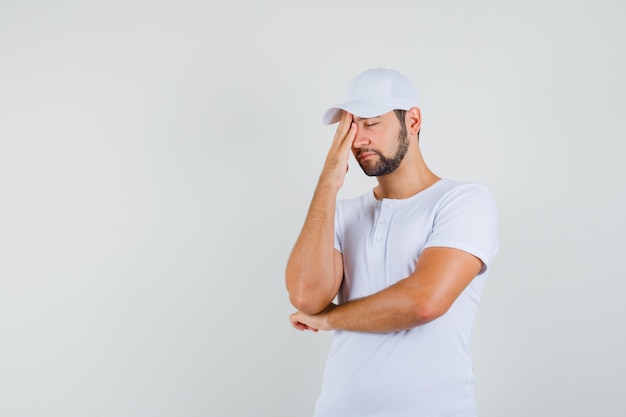 Free Photo young man in white t-shirt rubbing his forehead and looking sleepy , front view. free space for your text