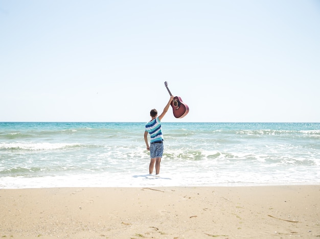 young man with acoustic guitar on the beach, joyful emotions, the concept of leisure and music