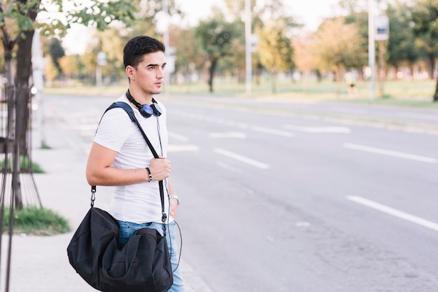 Young man with bag standing on roadside