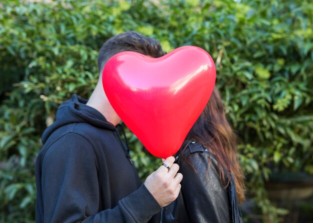 Young man with balloon in form of heart kissing woman 