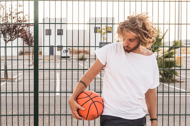 Free photo young man with basketball standing against fence