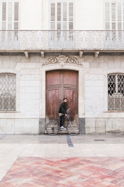 Free Photo young man with bicycle standing in front of vintage building