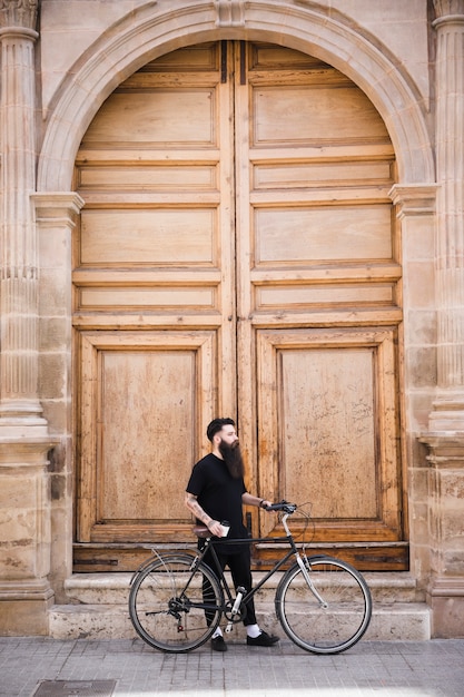 Free Photo young man with bicycle standing near the closed vintage door