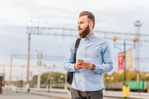 Young man with cellphone standing at railway station