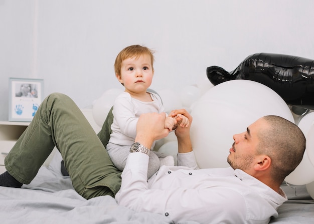 Free photo young man with little baby playing on bed near balloons