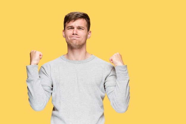 The young man with a raised fists on yellow studio background