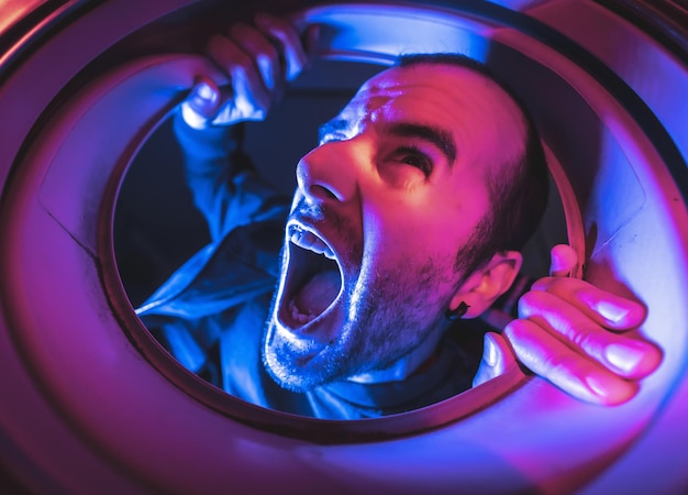 Free photo young man with a scared face looking into the washing machine