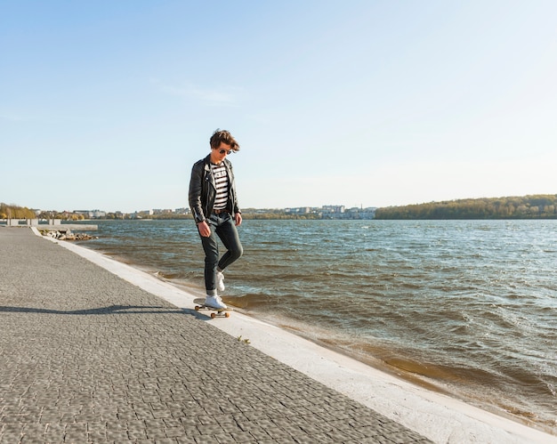 Free photo young man with a skateboard near the sea