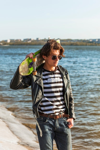 Free photo young man with a skateboard near the sea