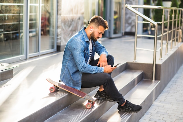 Free photo young man with skateboard using mobile phone