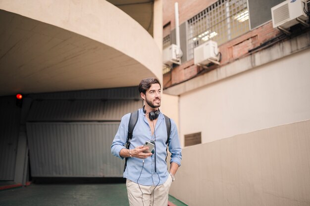 Young man with smartphone standing near building