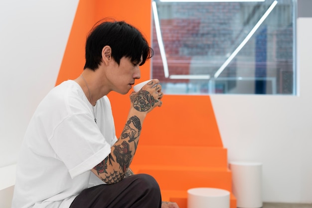 Free Photo young man with tattoos enjoying a cup of coffee at coffeehouse