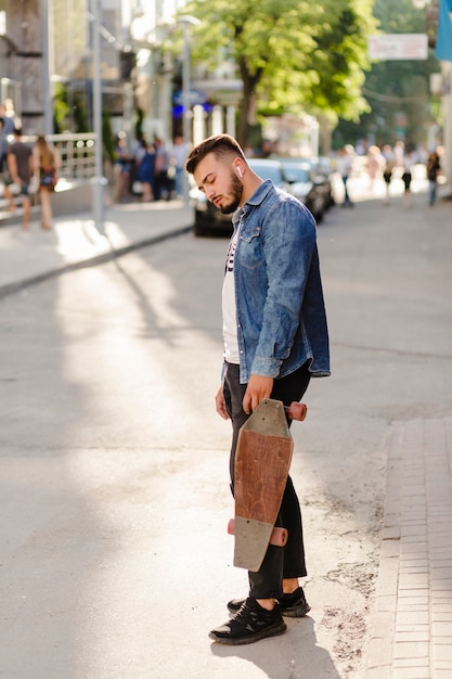 Young man with wooden skateboard standing on street