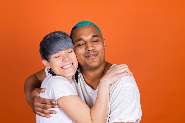 Free Photo young man and woman in casual white on orange wall hugging each other holding tight