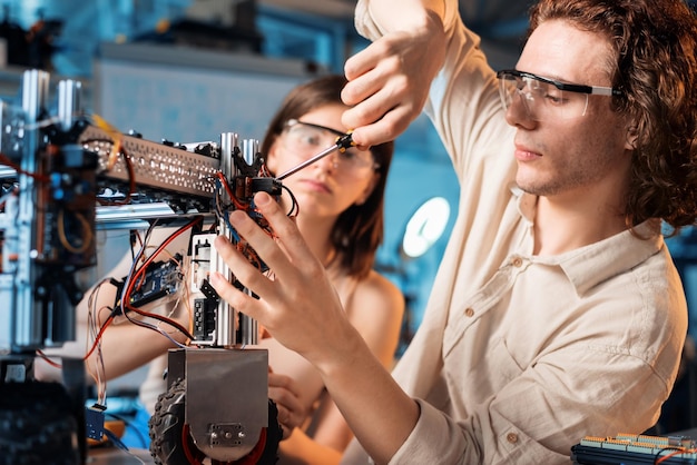 Free photo young man and woman in protective glasses doing experiments in robotics in a laboratory robot