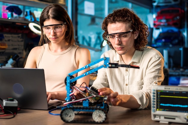 Free photo young man and woman in protective glasses doing experiments in robotics in a laboratory