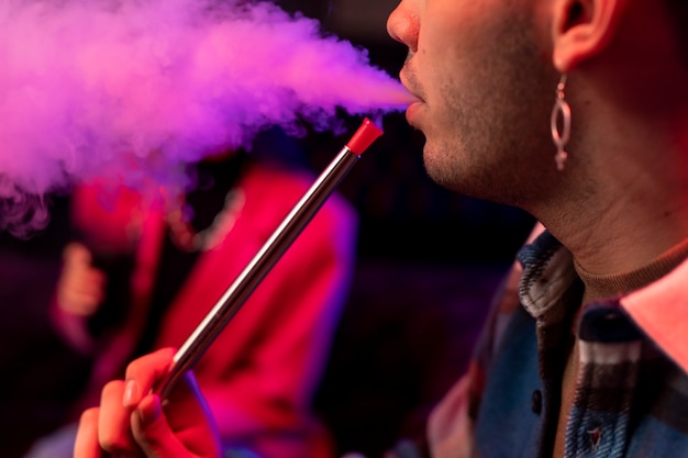 Free Photo young man and woman vaping from a hookah indoors