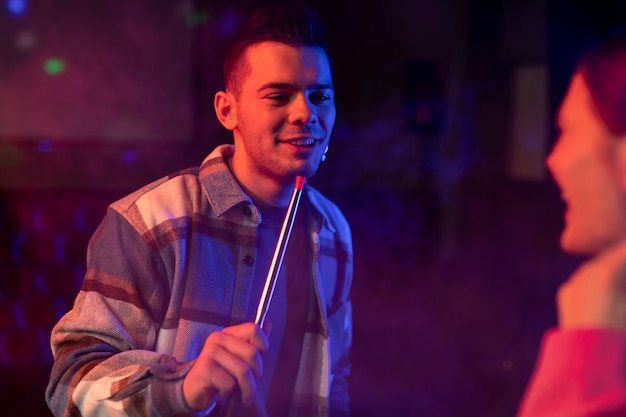 Young man and woman vaping from a hookah indoors