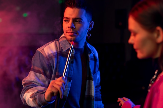 Young man and woman vaping from a hookah indoors