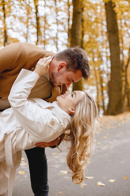 Free photo young man and woman walking outside wearing beige coats. blond woman and brunette man in autumn forest. romantic couple kissing.