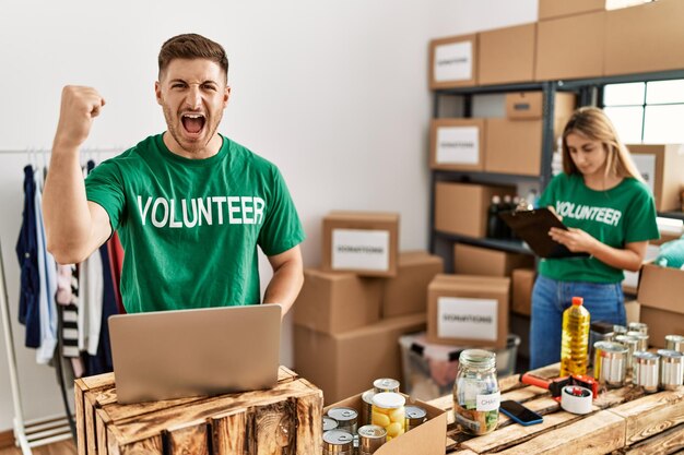 Young man and woman wearing volunteer t shirt at donations stand annoyed and frustrated shouting with anger, yelling crazy with anger and hand raised