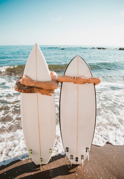 Free photo young man and woman with surf boards on coast near sea