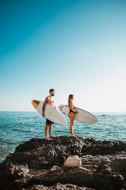 Young man and woman with surf boards on stone near sea