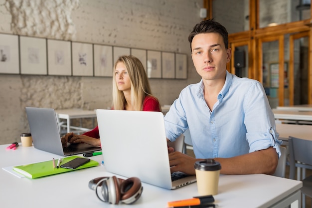 Young man and woman working on laptop in open space co-working office room,