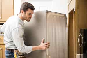 Free photo young man working as an electrician exposing the back of a fridge to check and repair it