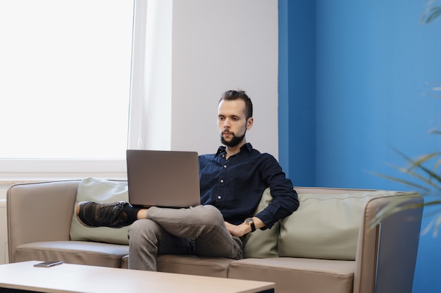 Young man working on the laptop while sitting on the sofa in the office